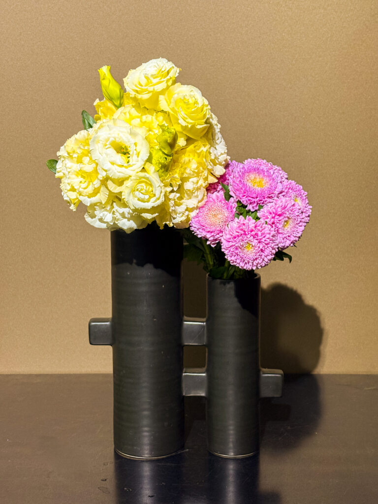 トルコキキョウとキクを使った、生け花とフラワーアレンジメントの融合作品。モダンな二連筒型花器に、左右対比で花をまとめた構成。
Ikebana arrangement with lisianthus and chrysanthemums in a modern dual-cylinder vase, blending traditional ikebana and floral arrangement styles.