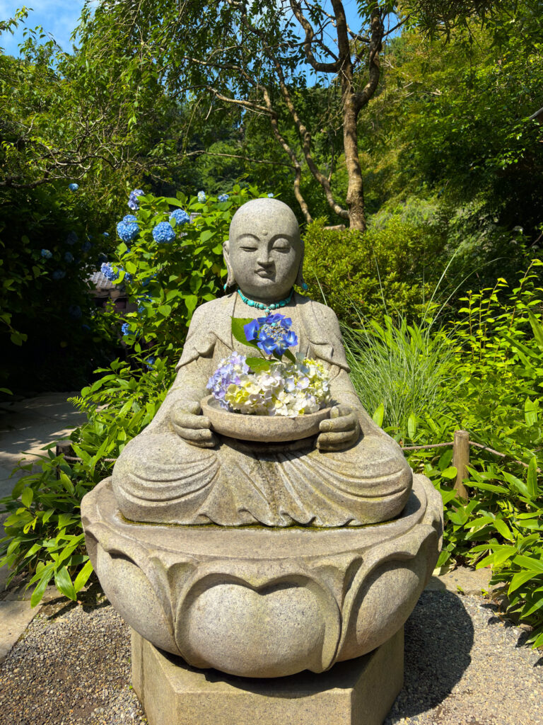 紫陽花を抱える穏やかな表情の明月院の地蔵像 / Peaceful Jizo statue holding hydrangeas at Meigetsuin Temple