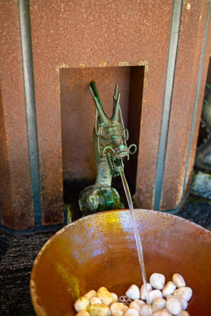 永平寺の龍の口から水が流れる手水舎。茶色の鉢に白い玉石が入っている。
