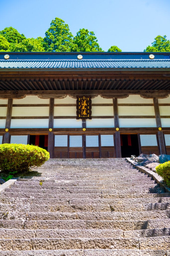 永平寺の法堂へと続く石段。青空と杉木立を背景にした荘厳な佇まい
