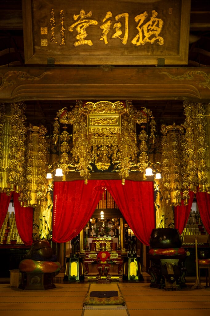 永平寺の法堂内の荘厳な本尊と金色の装飾、赤い幕に包まれた神聖な空間
