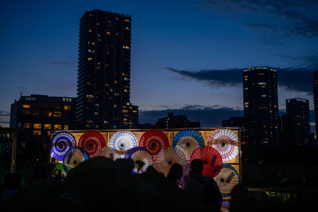 上野公園の夜に浮かび上がる和傘のライトアップと高層ビルの夜景

